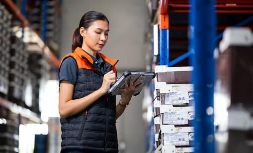 Using Cloud-Based Inventory Management and Tracking System. Female Manager using digital tablet in a factory warehouse while checking and tracking inventory real time data in ERP Software.